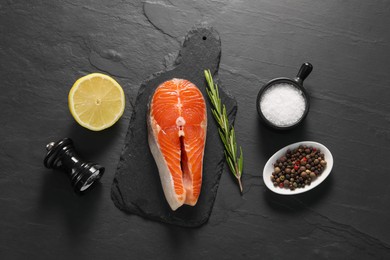 Photo of Fresh salmon steak, rosemary, lemon and spices on dark textured table, flat lay