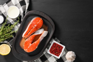 Photo of Fresh salmon steaks, lemon and spices on black wooden table, flat lay. Space for text