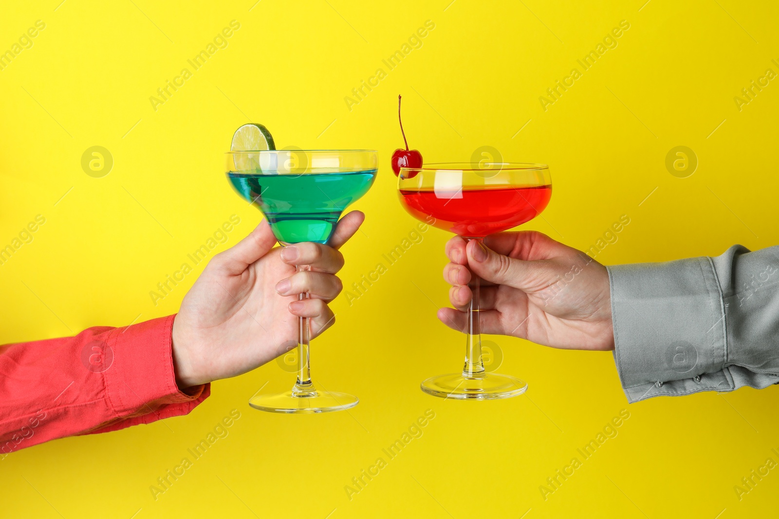 Photo of Friends with glasses of refreshing cocktails on yellow background, closeup