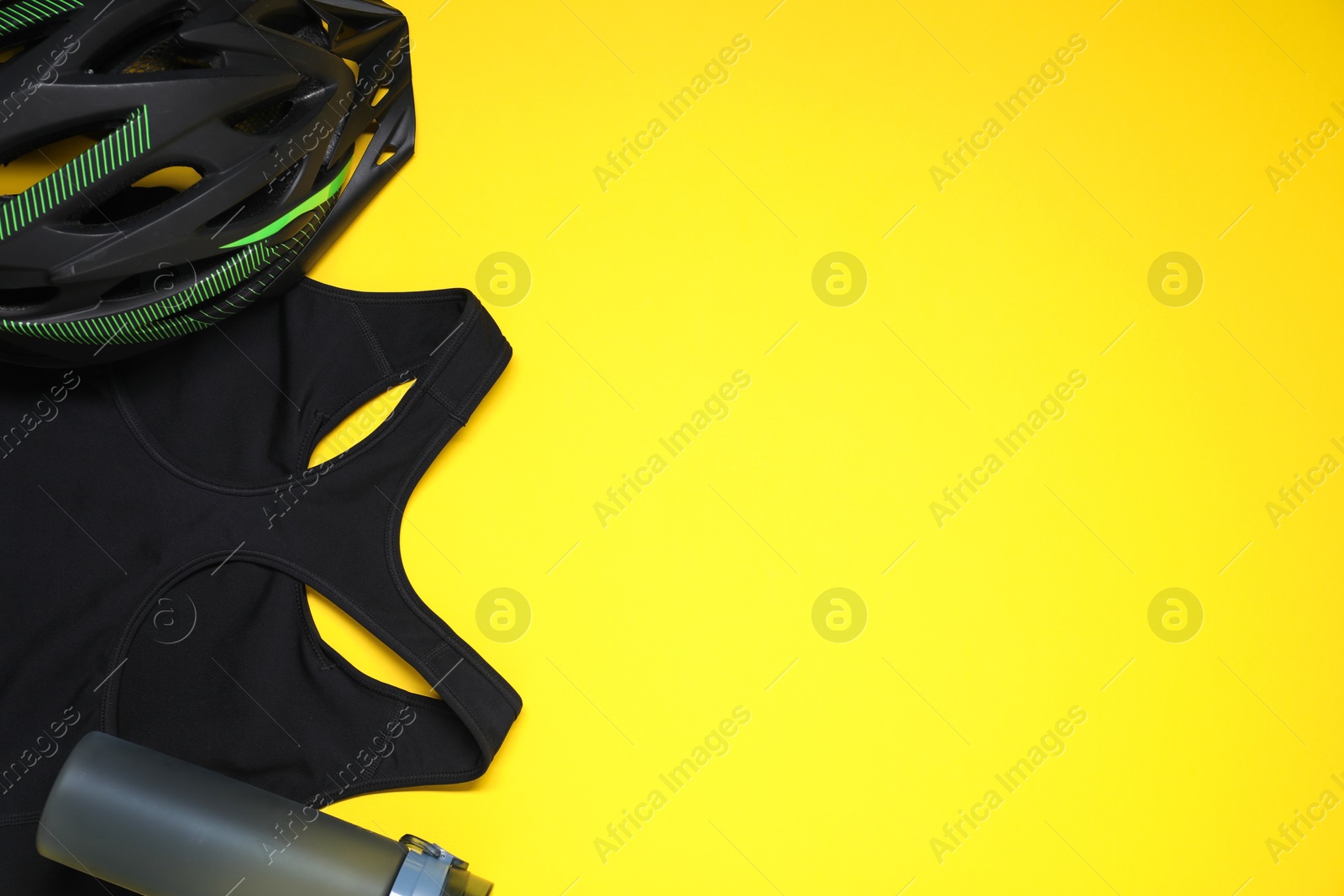 Photo of Bicycle helmet, sports bra and thermo bottle on yellow background, flat lay. Space for text