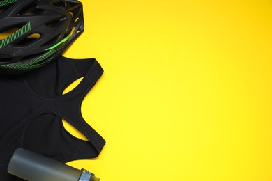 Bicycle helmet, sports bra and thermo bottle on yellow background, flat lay. Space for text