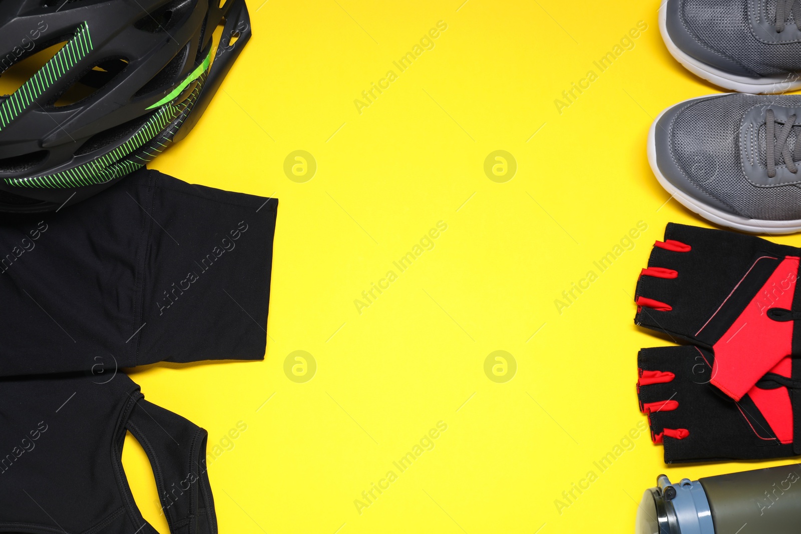 Photo of Bicycle helmet, sportswear, sneakers and thermo bottle on yellow background, flat lay. Space for text