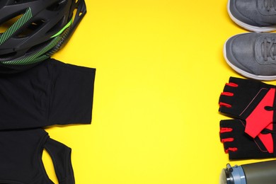 Photo of Bicycle helmet, sportswear, sneakers and thermo bottle on yellow background, flat lay. Space for text