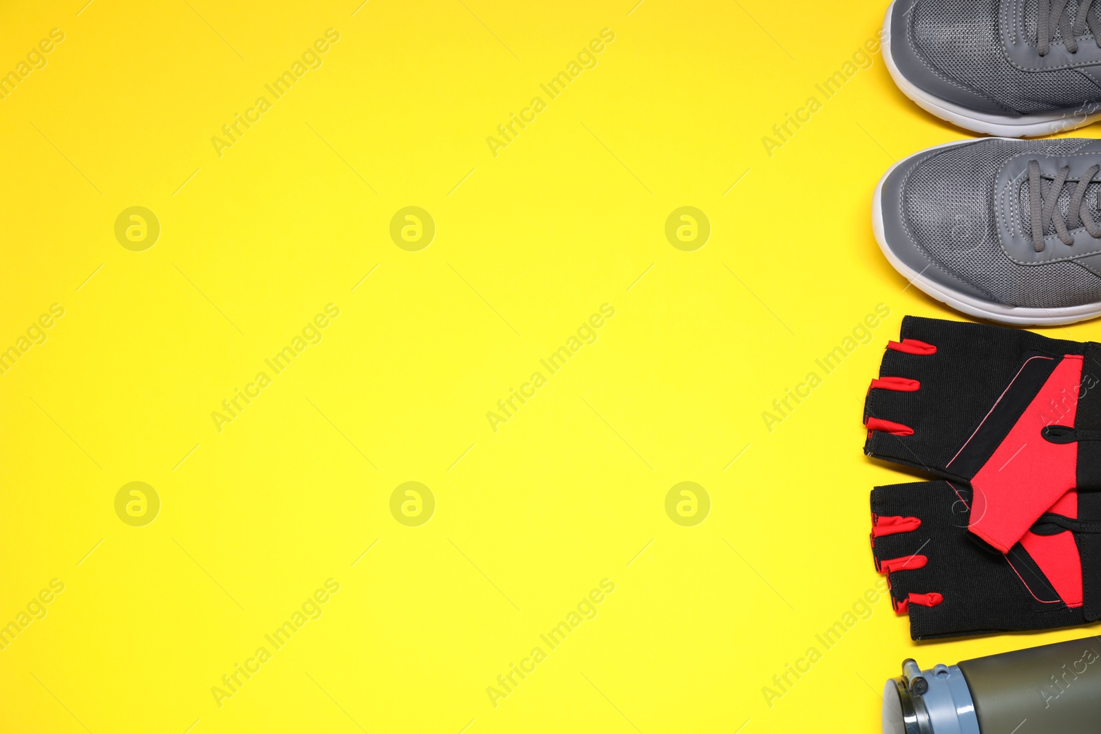 Photo of Fingerless cycling gloves, sneakers and thermo bottle on yellow background, flat lay. Space for text