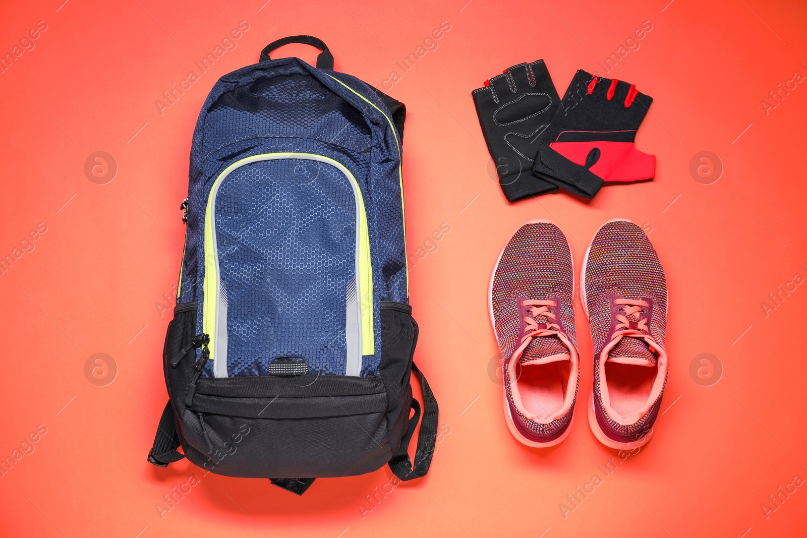 Photo of Backpack, fingerless cycling gloves and sneakers on coral background, flat lay