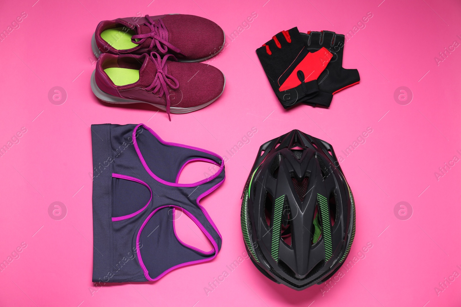 Photo of Bicycle helmet, sports bra, sneakers and fingerless gloves on pink background, flat lay