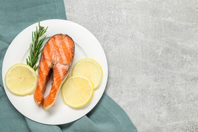 Photo of Tasty grilled salmon steak, lemon and rosemary on gray textured table, top view. Space for text