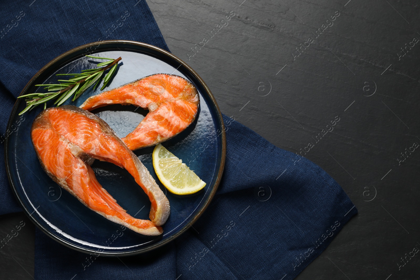 Photo of Tasty grilled salmon steaks, lemon and rosemary on black textured table, top view. Space for text