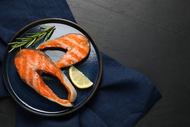 Photo of Tasty grilled salmon steaks, lemon and rosemary on black textured table, top view. Space for text