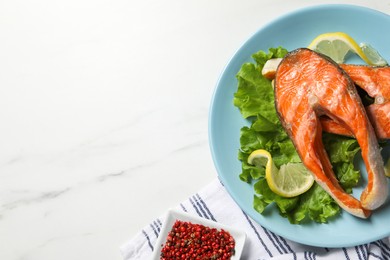 Photo of Tasty grilled salmon steaks, lettuce, lemon and spices on white marble table, flat lay. Space for text