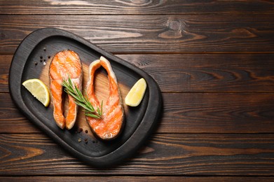 Photo of Tasty grilled salmon steaks, lemon and spices on wooden table, top view. Space for text