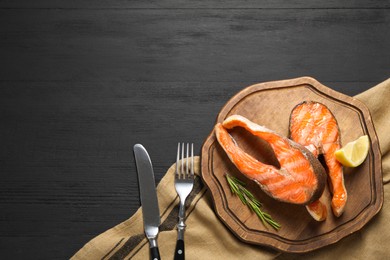 Photo of Tasty grilled salmon steaks served on black wooden table, flat lay. Space for text