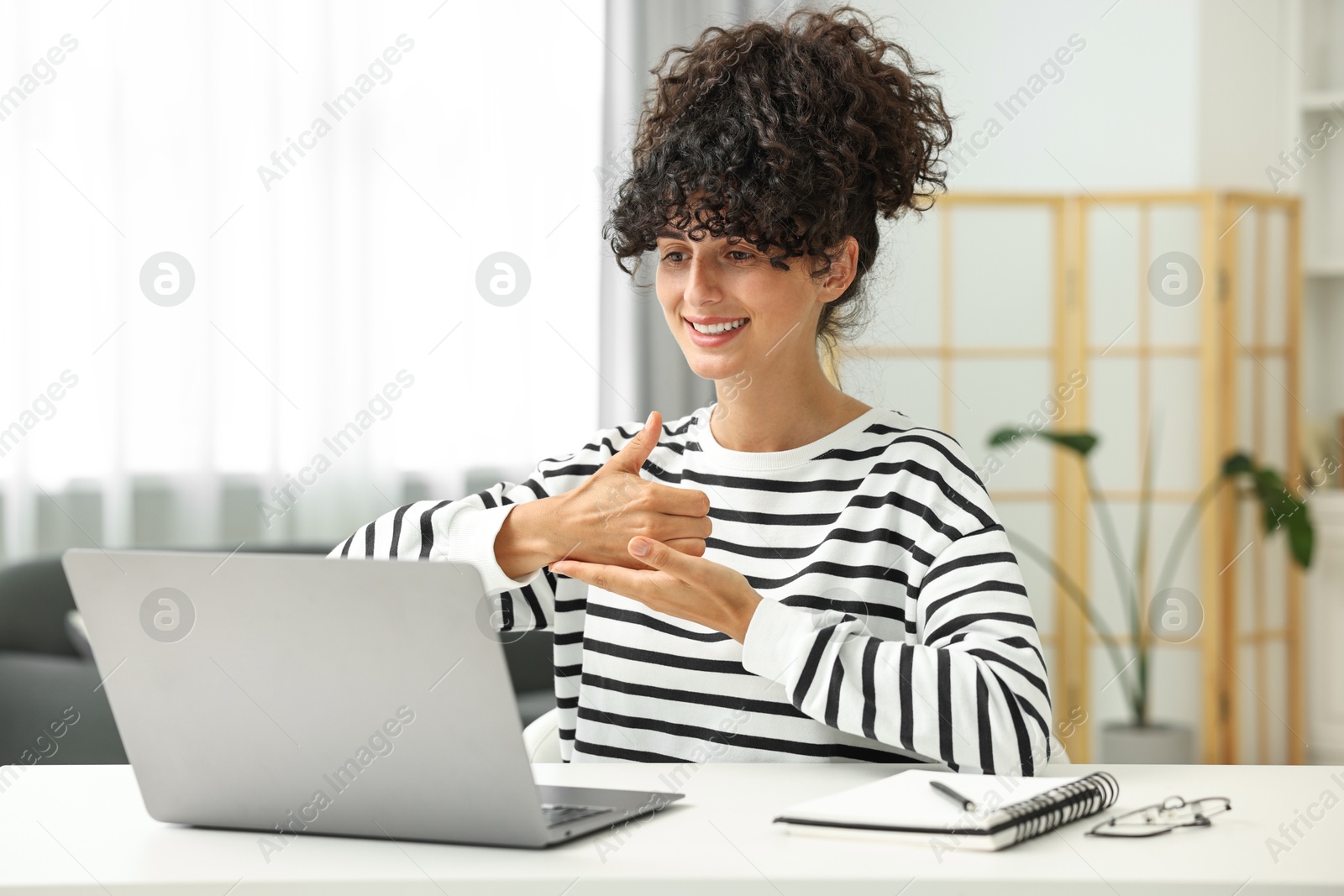 Photo of Young woman using sign language for communication during video call at white table indoors