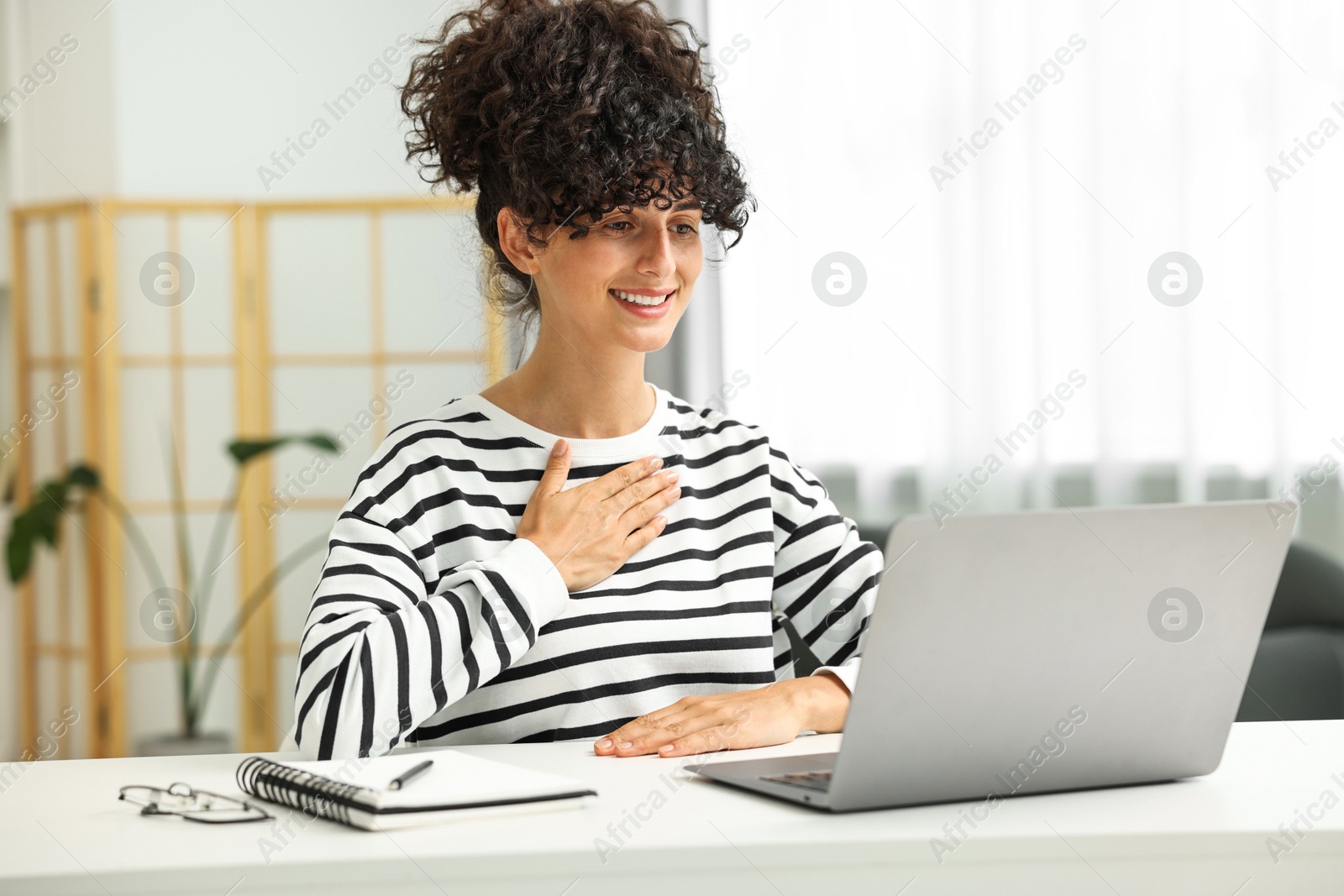 Photo of Young woman using sign language for communication during video call at white table indoors