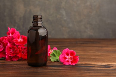 Photo of Geranium essential oil in bottle and beautiful flowers on wooden table, space for text