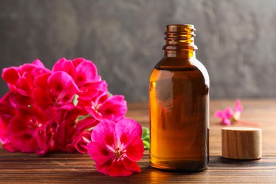 Photo of Geranium essential oil in bottle and beautiful flowers on wooden table