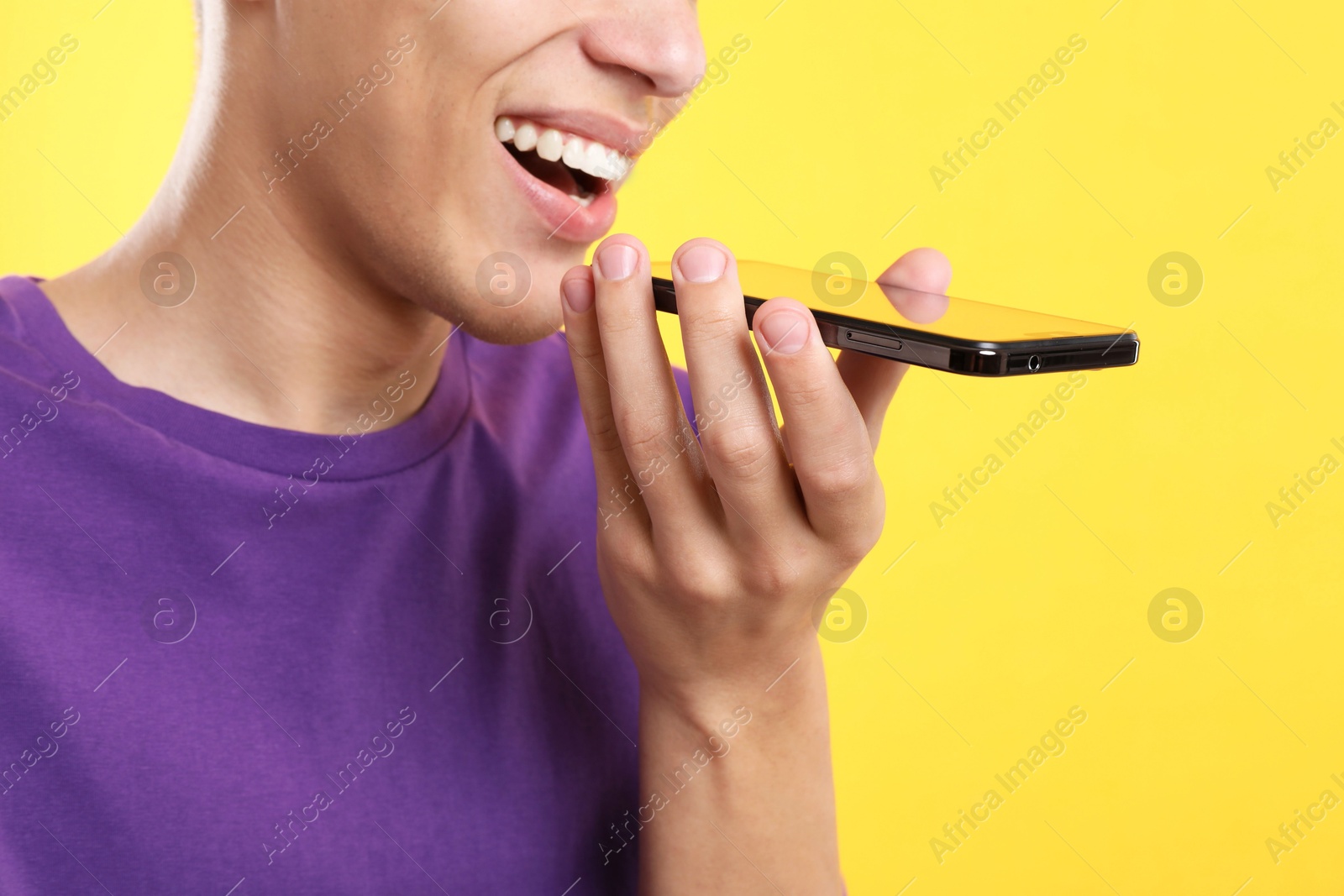 Photo of Young man recording voice message via smartphone on yellow background, closeup