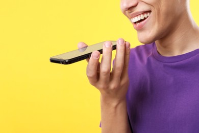 Young man recording voice message via smartphone on yellow background, closeup. Space for text