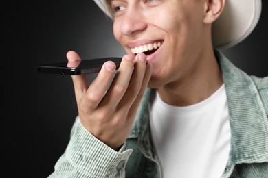 Photo of Young man recording voice message via smartphone on dark background, selective focus