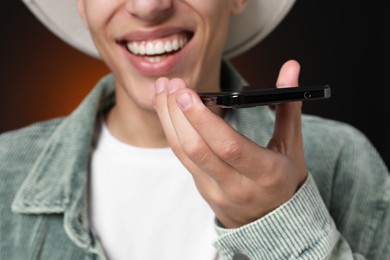 Photo of Young man recording voice message via smartphone on dark background, closeup