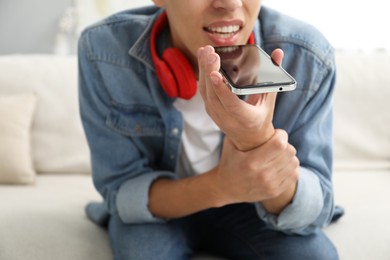 Photo of Young man recording voice message via smartphone at home, closeup