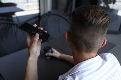 Photo of Young man with smartphone listening to voice message in outdoor cafe, back view