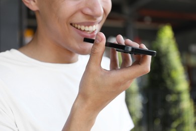 Photo of Young man recording voice message via smartphone outdoors, closeup