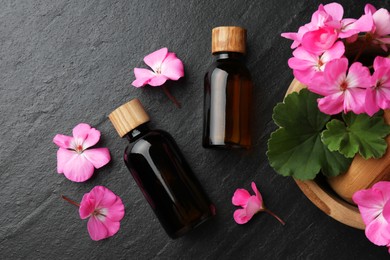 Photo of Bottles of geranium essential oil, beautiful flowers and mortar with pestle on black table, flat lay