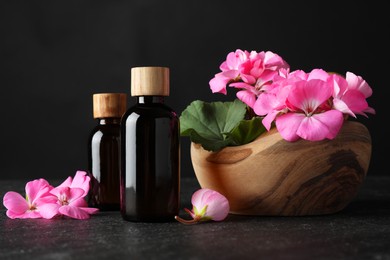 Photo of Bottles of geranium essential oil and beautiful flowers on black table