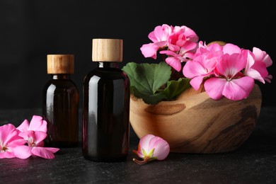 Photo of Bottles of geranium essential oil and beautiful flowers on black table, closeup