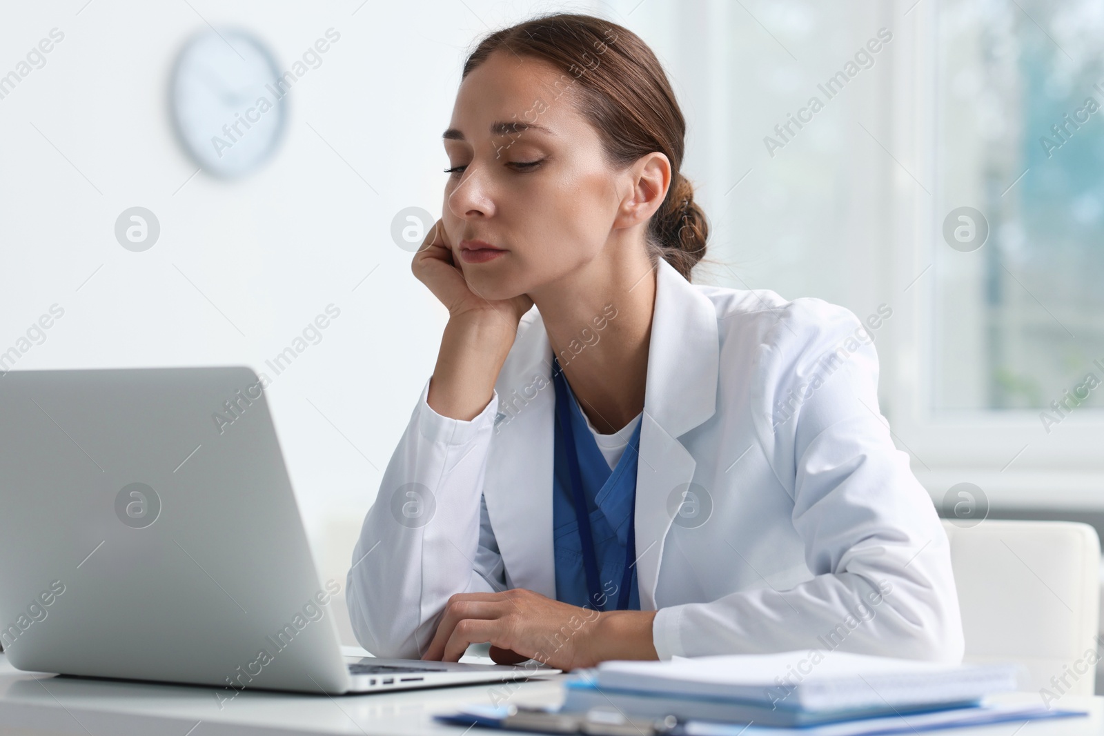 Photo of Sleepy nurse at white table with laptop in clinic