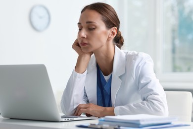 Sleepy nurse at white table with laptop in clinic