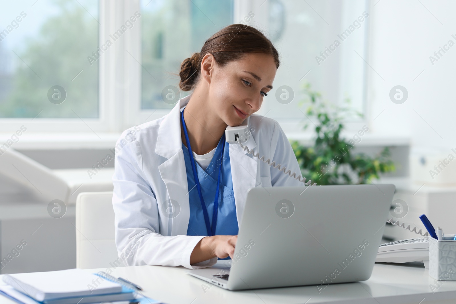 Photo of Nurse consulting patient by phone at white table in clinic