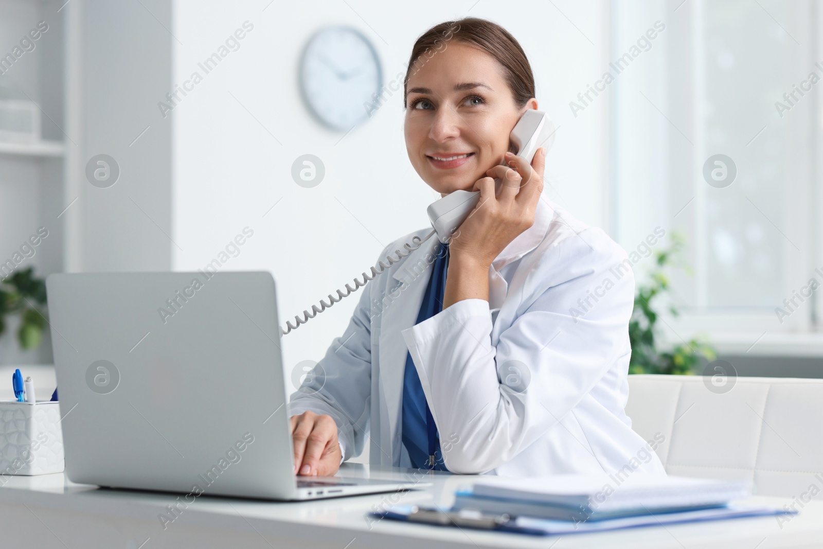 Photo of Nurse consulting patient by phone at table in clinic