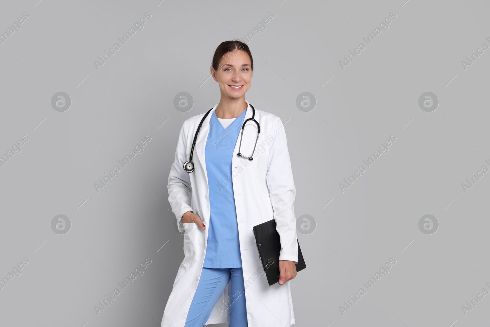 Photo of Nurse in medical uniform with stethoscope and clipboard on grey background