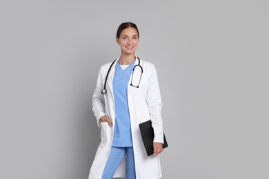 Nurse in medical uniform with stethoscope and clipboard on grey background