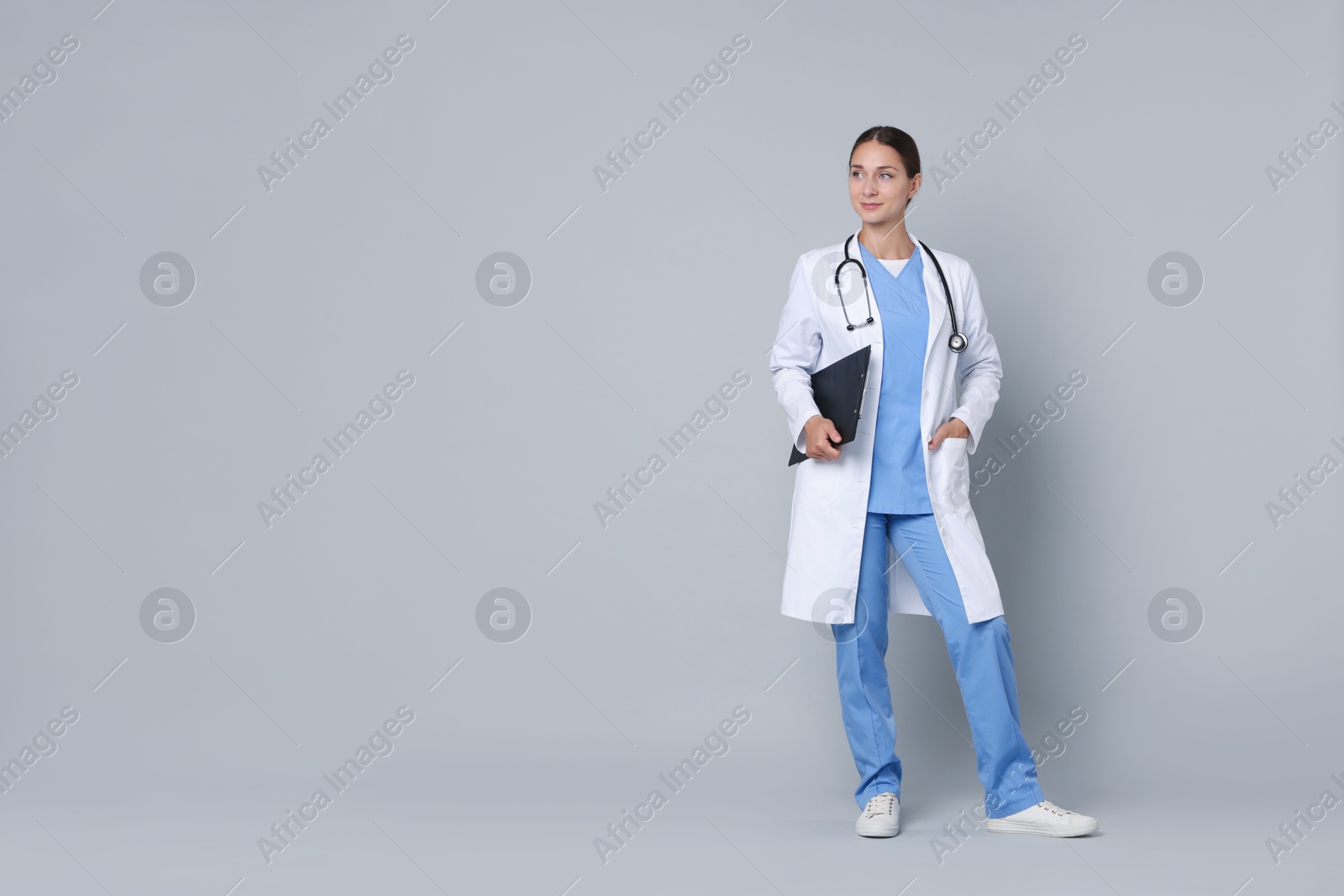 Photo of Nurse in medical uniform with stethoscope and clipboard on grey background, space for text