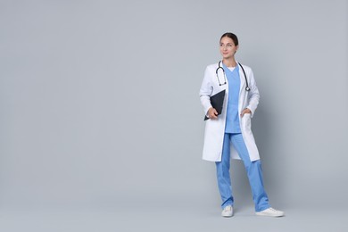 Nurse in medical uniform with stethoscope and clipboard on grey background, space for text