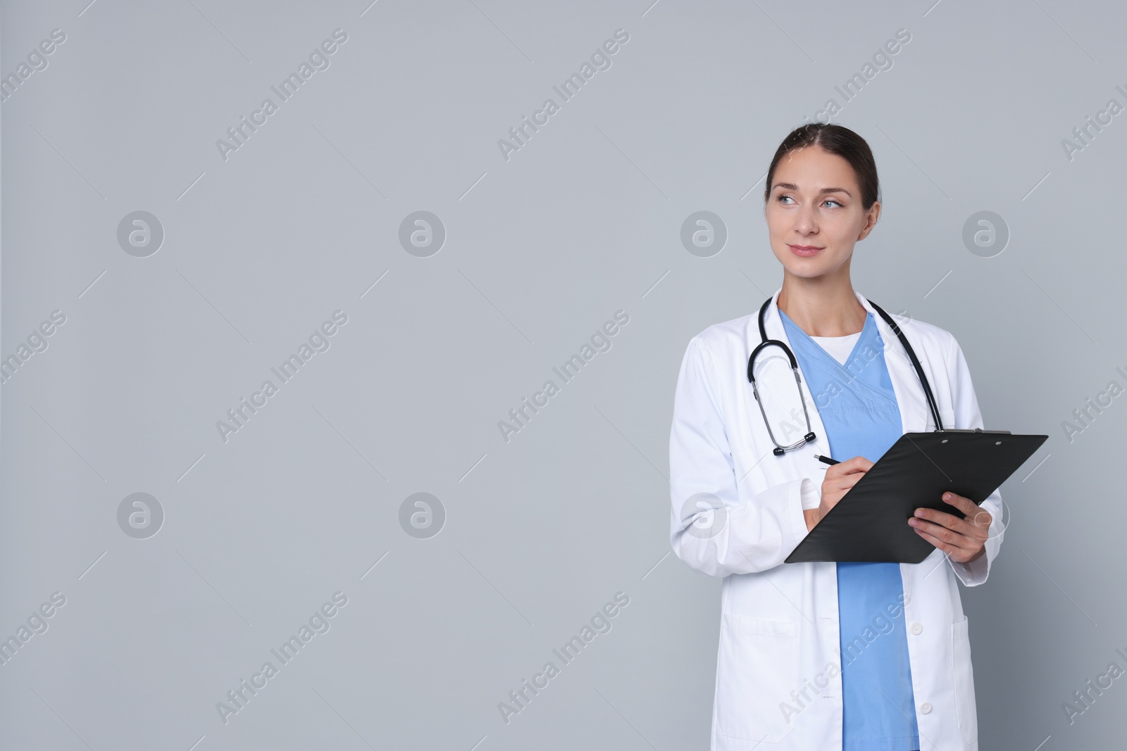 Photo of Nurse in medical uniform with stethoscope and clipboard on grey background, space for text