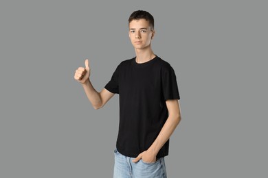 Photo of Teenage boy wearing black t-shirt and showing thumbs up on grey background