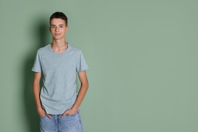 Teenage boy wearing light grey t-shirt on green background, space for text