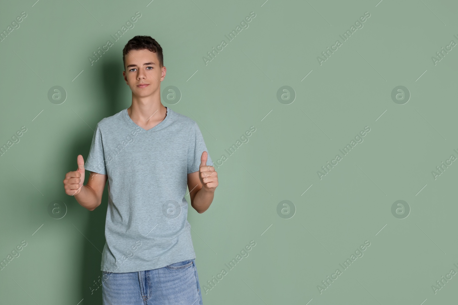 Photo of Teenage boy wearing light grey t-shirt and showing thumbs up on green background, space for text