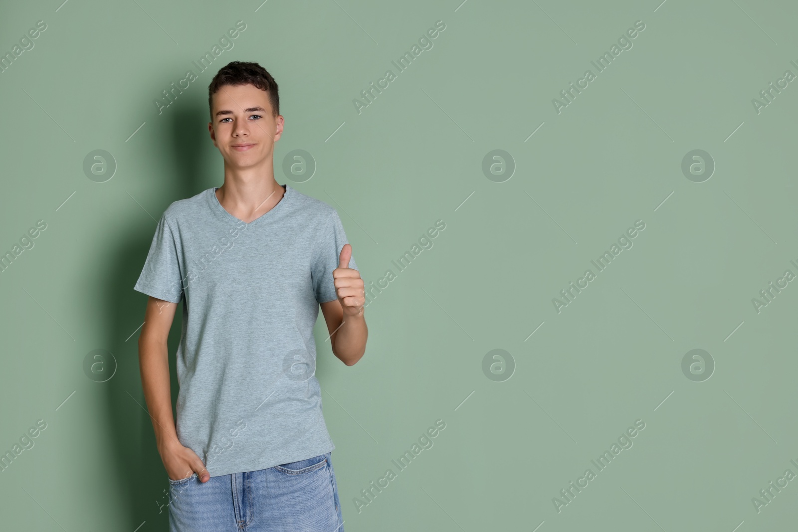 Photo of Teenage boy wearing light grey t-shirt and showing thumbs up on green background, space for text