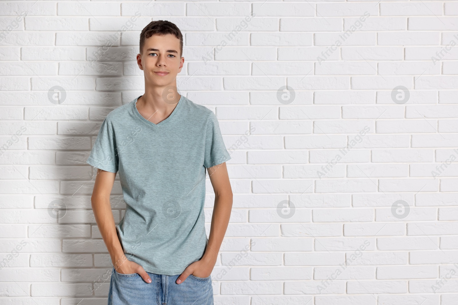 Photo of Teenage boy wearing grey t-shirt near white brick wall, space for text