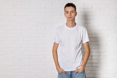 Teenage boy wearing t-shirt near white brick wall, space for text