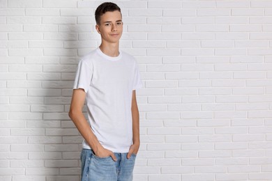 Photo of Teenage boy wearing t-shirt near white brick wall, space for text