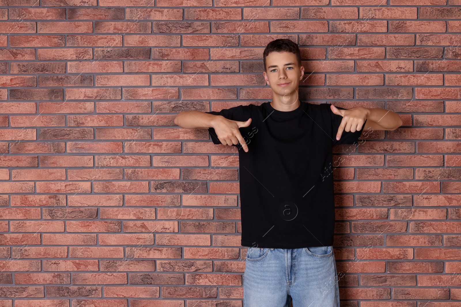 Photo of Teenage boy wearing black t-shirt near brick wall, space for text