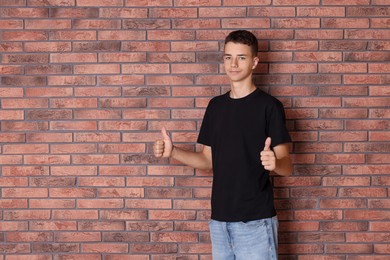 Photo of Teenage boy wearing black t-shirt and showing thumbs up near brick wall