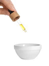 Photo of Woman dripping tincture from pipette into bowl on white background, closeup