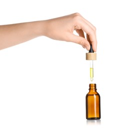 Photo of Woman dripping tincture from pipette into bottle on white background, closeup